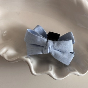 Detail view of a light blue fabric bow hair clip with textured weave on a white tray