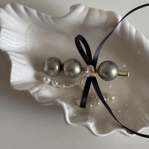 Detail of elegant hair clip with grey pearls, black ribbon bow and a heart gemstone