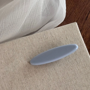 Detail view of the light blue matte oval hair claw clip on a textured beige surface