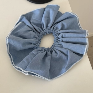 Detail of light blue denim texture scrunchie with white stitching edges and elastic band