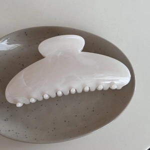 Macro view of large pearl white acetate hair claw clip with marble ink texture on ceramic plate