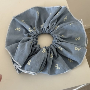 Detail of grey-blue scrunchie featuring white bow patterns and fine stitched edges