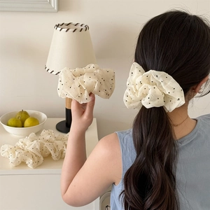 Detail of cream organza polka dot scrunchie worn on ponytail in cozy home setting