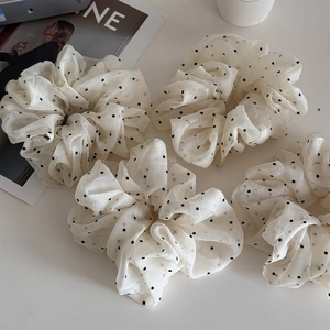 Close-up of cream polka dot organza hair scrunchies on a minimalist background