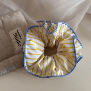 Vue détaillée d'un chouchou en tissu rayé jaune et blanc avec bordure bleue fine