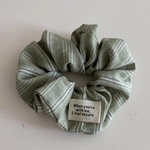Detail of green pinstripe fabric scrunchie with letter patch and cotton texture