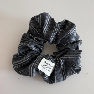 Detail of grey striped fabric scrunchie featuring a white patch with secure text
