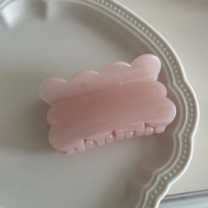 Detail einer rosa gewellten Haarklammer mit Perlglanz-Finish auf einem weißen Teller