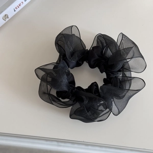 Detailansicht eines schwarzen Organza-Haargummis mit Lagenfalten auf weißer Fläche