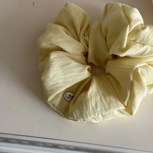 Detail shot of a soft yellow scrunchie with a cute bow motif button on a white surface