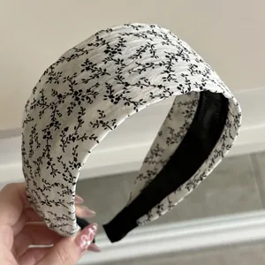 Close-up of wide padded headband featuring black floral patterns on white fabric