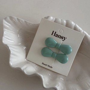 Pair of mini light green bow hair clips displayed on a white shell decorative tray