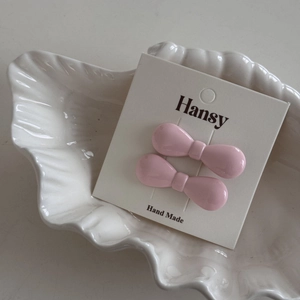 Close-up of two mini pink bow hair clips on a decorative white shell tray