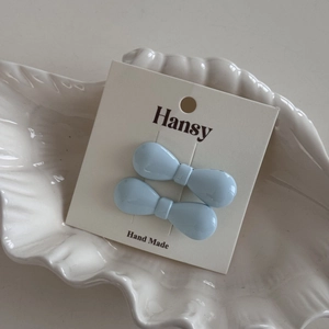 Pair of light blue bow hair clips on display card inside a white ceramic shell tray