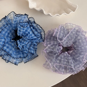 Blue and purple oversized mesh plaid scrunchies with ruffled edges on cream surface