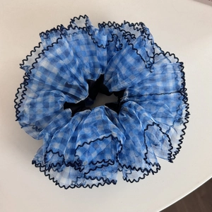Detail of blue gingham mesh scrunchie with black wavy edges and semi-transparent fabric