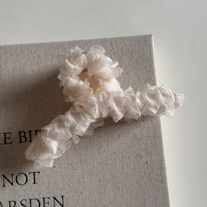 Détail du tissu en maille plissée crème et pince métallique sur une pince à cheveux