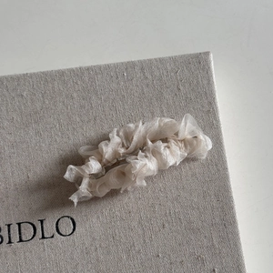 Détail d'une pince à cheveux en organza plissé couleur champagne au design ondulé
