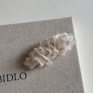 Détail montrant les couches de tulle plissé crème et la texture fine de la pince à cheveux
