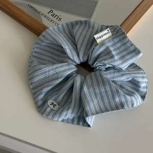 Close-up of blue striped scrunchie with Happiness label and bow-knot button detail