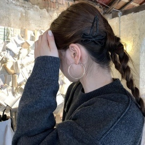Detail of large silver hoop earrings and black bow hair clip on a model's braided hair