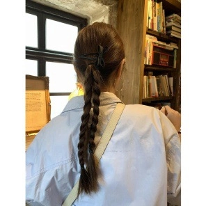 Elegant black silk ribbon bow hair clip styled on a braided ponytail in a library setting