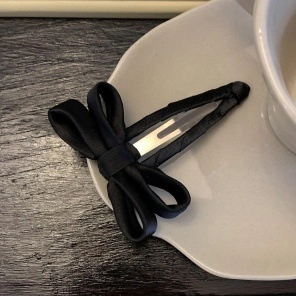 Detailed shot of large black satin ribbon hair clip on elegant white porcelain plate