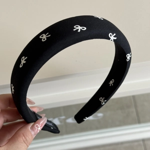 Gros plan du serre-tête rembourré noir avec motifs nœuds blancs et étiquette en tissu