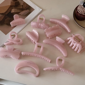 Pink pearlescent hair claw clips in various shapes like hearts and bows on a minimalist table