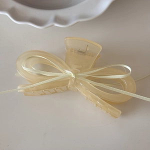 Close-up of cream yellow resin ribbon bow hair claw clip on white porcelain plate