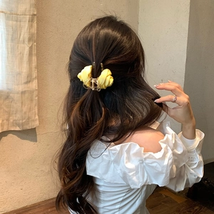 Dettaglio di una molletta per capelli a rosa gialla in tessuto con base in metallo dorato
