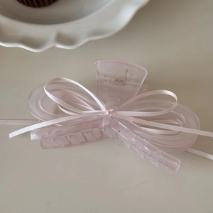 Macro view of large light pink bow hair claw clip with silk ribbon on a white ceramic plate