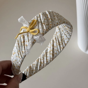 Detail van een bloemen scrunchie met gele print, wit kant en strikversiering