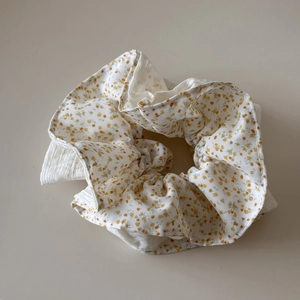 Detail van een stoffen scrunchie met gele bloemenprint op een witte getextureerde stof
