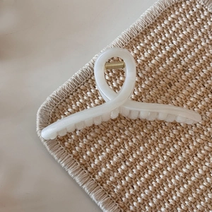 Detail of creamy white jelly hair claw clip with golden spring on woven mat