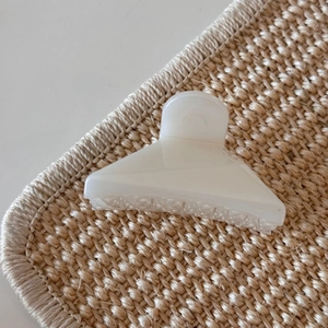 Detail view of cream jelly hair claw clip with subtle shimmer on a woven mat