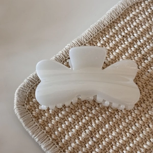 Close-up of translucent white hair claw clip with smooth texture on woven mat
