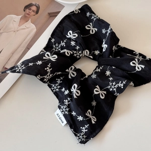 Close-up of black silk scrunchie with white bow embroidery and brand woven label