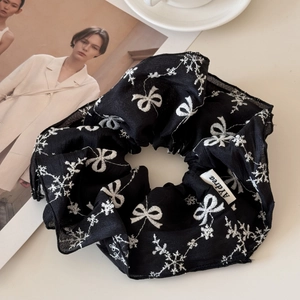 Detail of black ribbon scrunchie with white bow embroidery and brand woven label