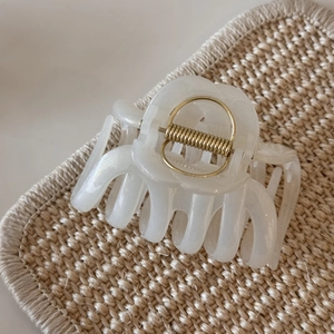 Detail of pearlescent cream hair claw clip with gold spring on a woven mat surface