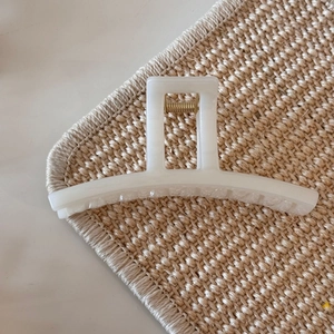 Close-up of a creamy white jelly hair claw clip with golden spring on woven mat