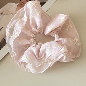 Close-up of pink organza scrunchie featuring elegant white flower and bow embroidery