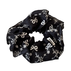 Elegant black scrunchie with white bow embroidery and texture detail on a white background