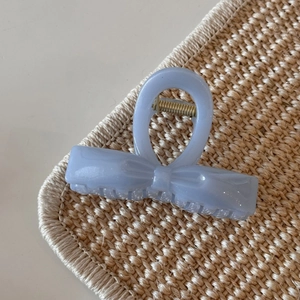 Detail of blue glitter bow hair claw clip with golden spring on woven mat texture