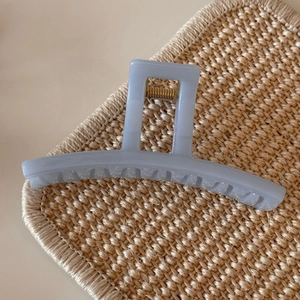 Close-up of translucent blue hair claw clip with golden metal spring on woven mat