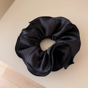Dettaglio di un grande elastico per capelli in raso nero con cuciture su sfondo beige