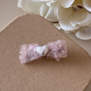 Vue détaillée d'un nœud en dentelle rose avec une perle en forme de cœur au centre du clip