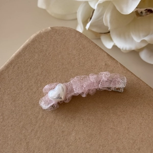 Gros plan d'une pince à cheveux en dentelle rose avec une perle de cœur blanche