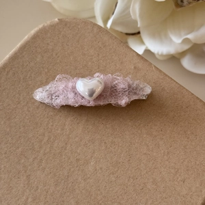 Détail d'une pince à cheveux en dentelle rose avec une perle blanche en cœur