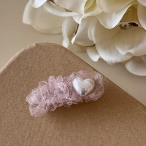 Détail d'une pince à cheveux en dentelle rose avec perle en cœur sur papier kraft